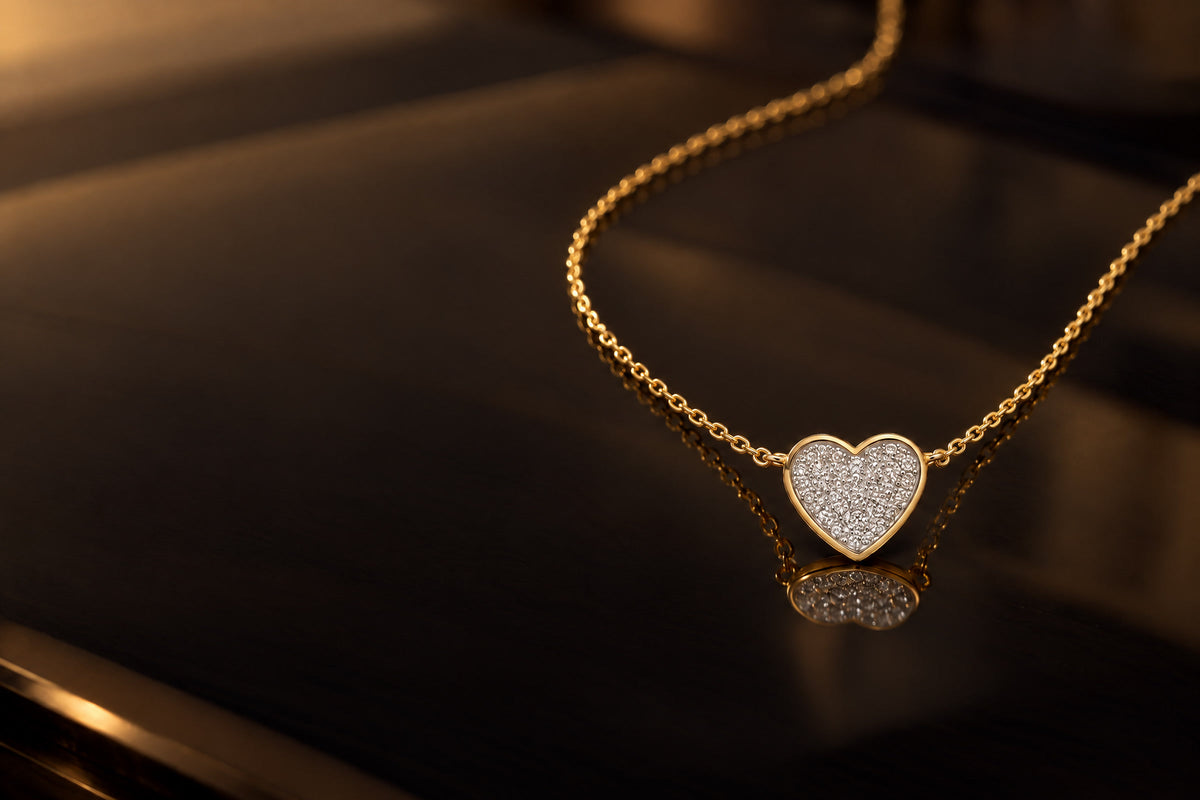 Collier aus Gelbgold mit Diamant-Herz liegt auf dunklem, warm beleuchtetem Rauchglas